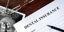 Dental insurance paperwork, X-ray, pen, and glasses on desk
