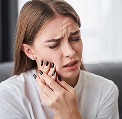 a woman holding her cheek due to failed dental implant