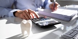 man using calculator with model tooth on his desk