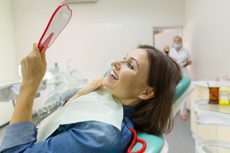 a middle-aged woman staring at her new smile while seated in the dentist’s chair