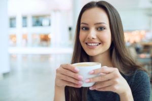 A woman smiling while drinking a cup of coffee