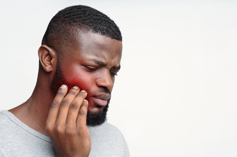 A man rubbing his jaw due to impacted wisdom tooth pain